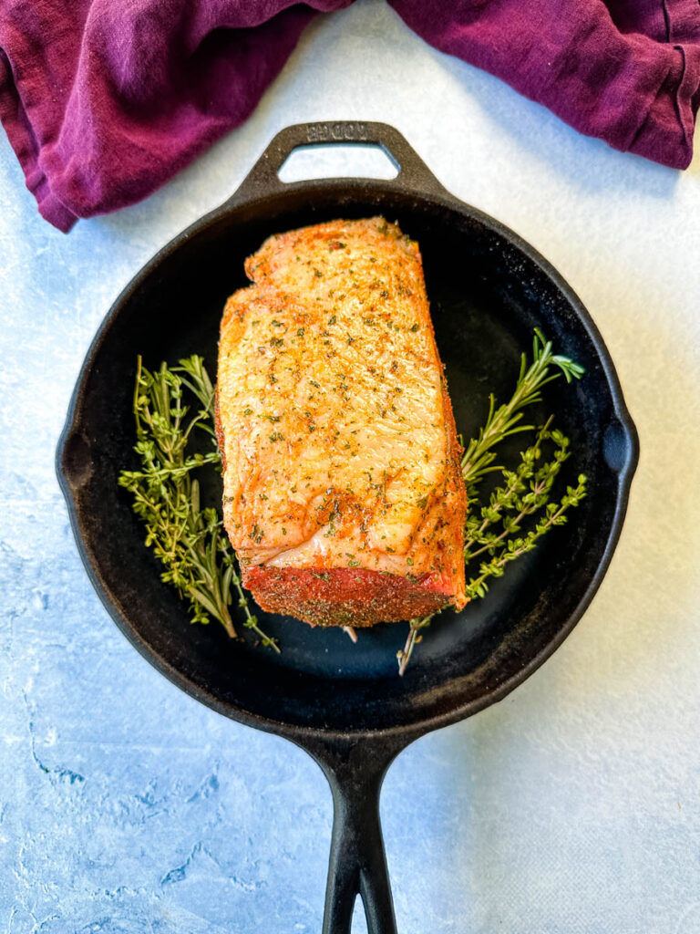 raw eye of round roast beef in a cast iron skillet with fresh herbs