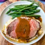 sliced eye of round roast beef on a plate with mashed potatoes, green beans, and au jus gravy