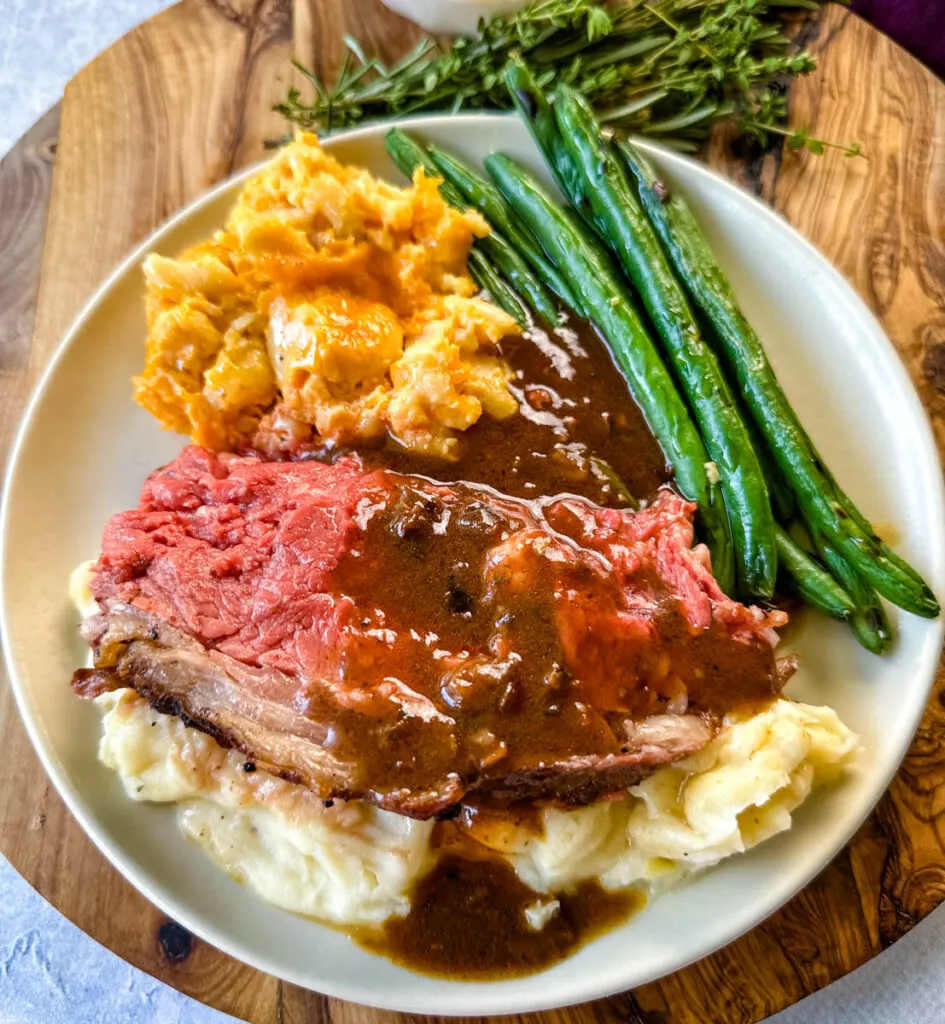 garlic herb butter roasted prime rib with au jus gravy on a plate with green beans, mashed potatoes, and mac and cheese