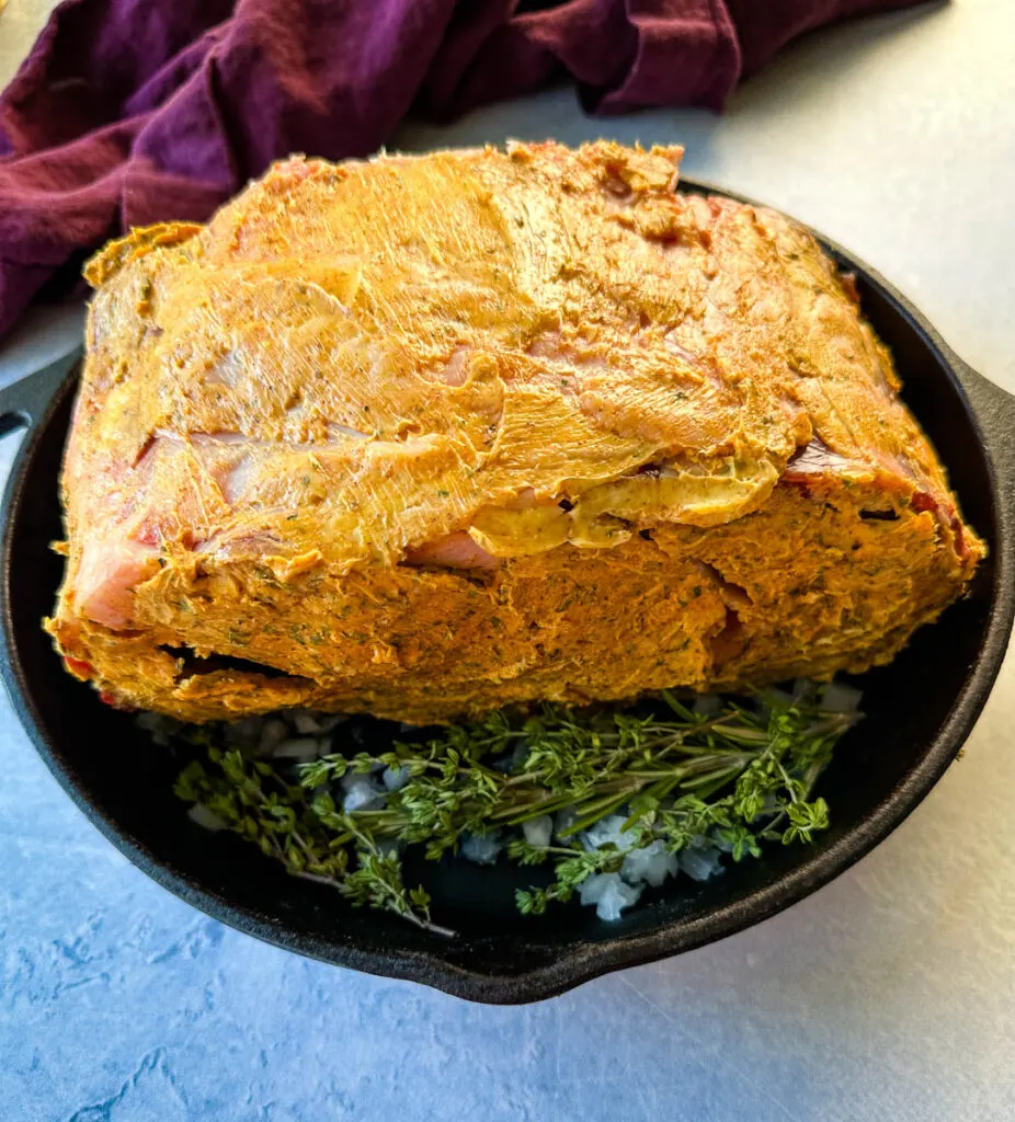 uncooked garlic herb butter roasted prime rib in a cast iron skillet with herbs