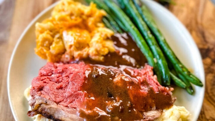 garlic herb butter roasted prime rib with au jus gravy on a plate with green beans, mashed potatoes, and mac and cheese