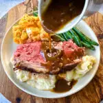 garlic herb butter roasted prime rib with au jus gravy on a plate with green beans, mashed potatoes, and mac and cheese