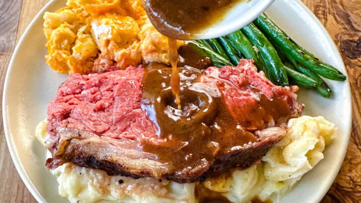 garlic herb butter roasted prime rib with au jus gravy on a plate with green beans, mashed potatoes, and mac and cheese