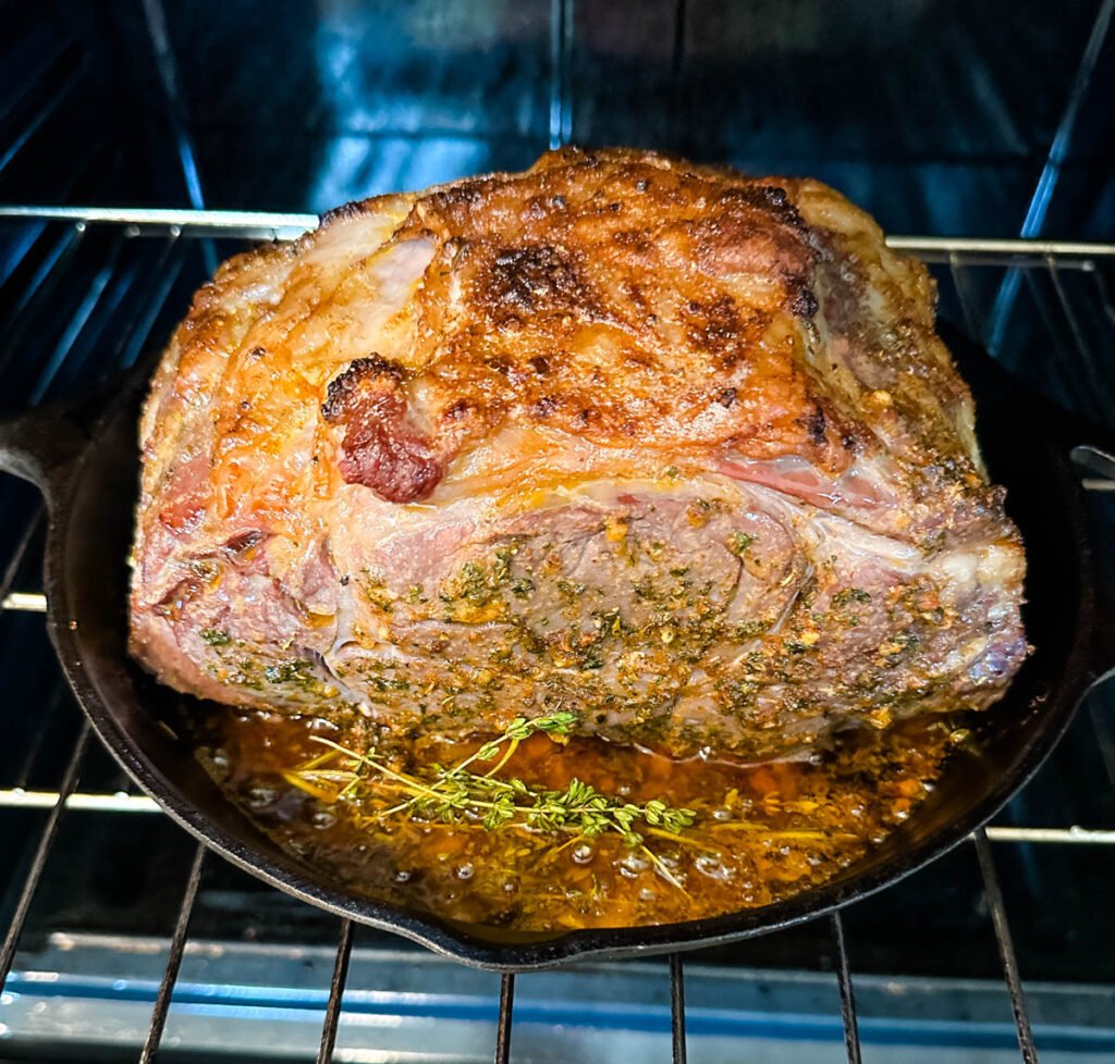 garlic herb butter roasted prime rib in a cast iron skillet with herbs in the oven