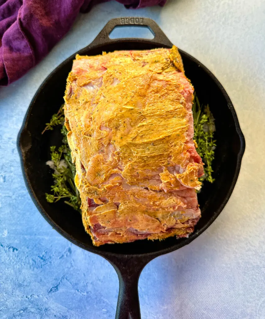 uncooked garlic herb butter roasted prime rib in a cast iron skillet with herbs