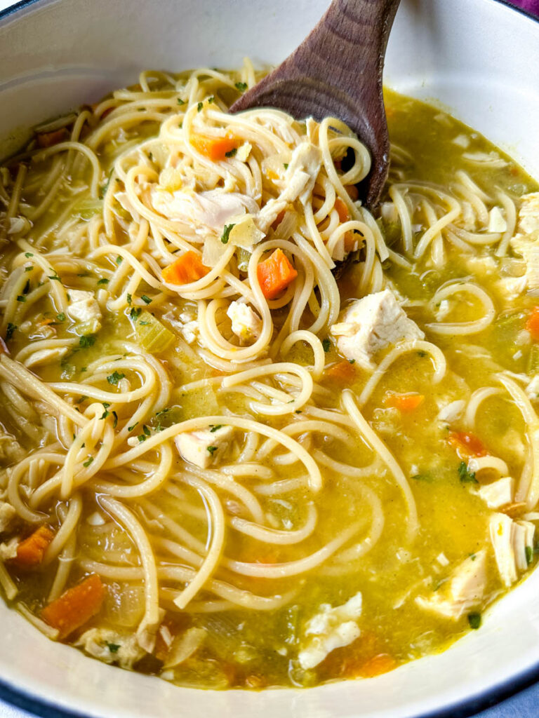rotisserie chicken noodle soup with carrots and celery in a Dutch oven with a wooden spoon