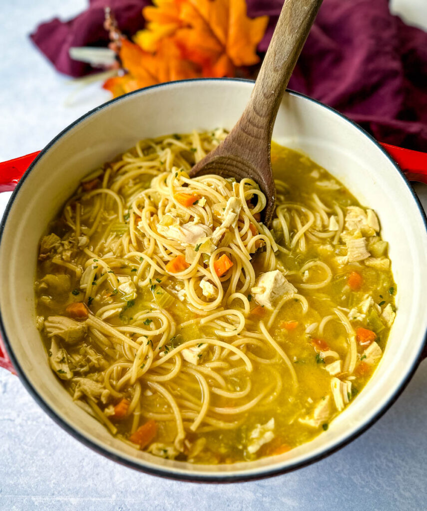 rotisserie chicken noodle soup with carrots and celery in a Dutch oven with a wooden spoon