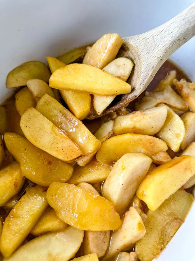 baked apples with cinnamon in a Crockpot slow cooker with a wooden spoon