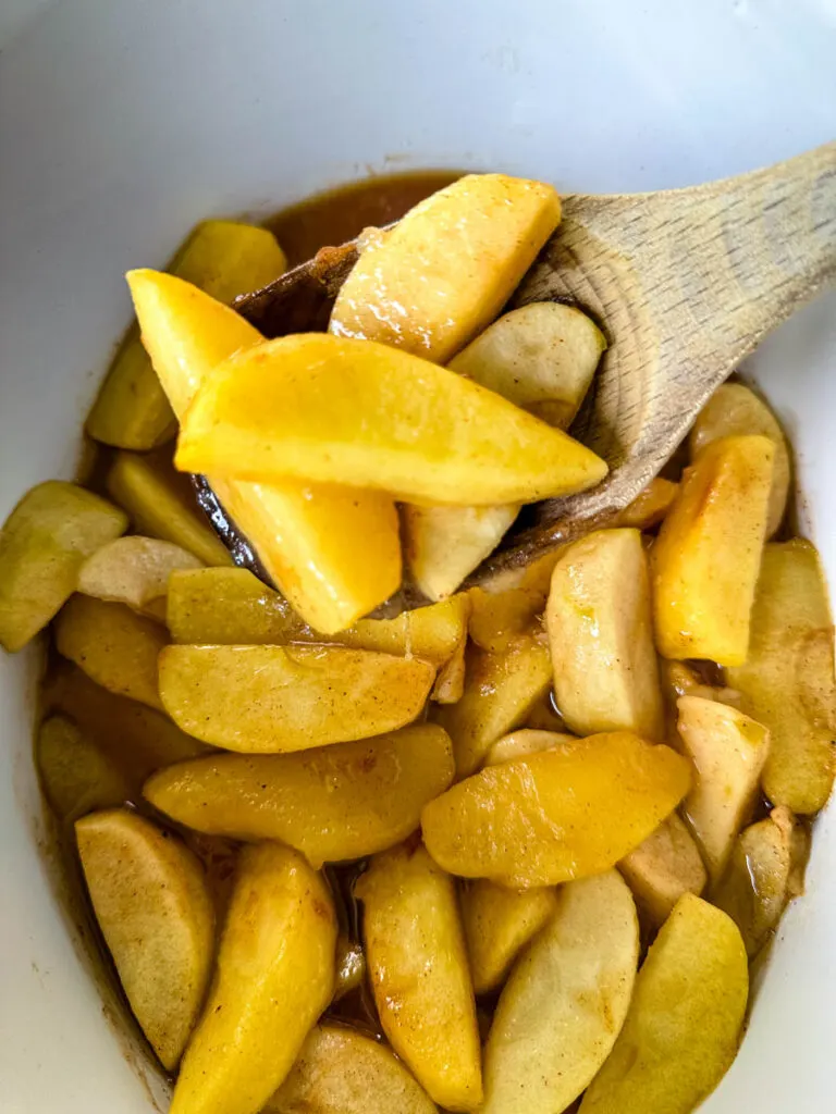 baked apples with cinnamon in a Crockpot slow cooker with a wooden spoon