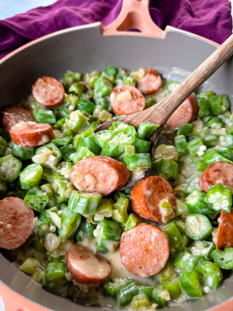 smothered okra with sausage and gravy in a skillet with a wooden spoon