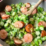 smothered okra with sausage and gravy in a skillet with a wooden spoon