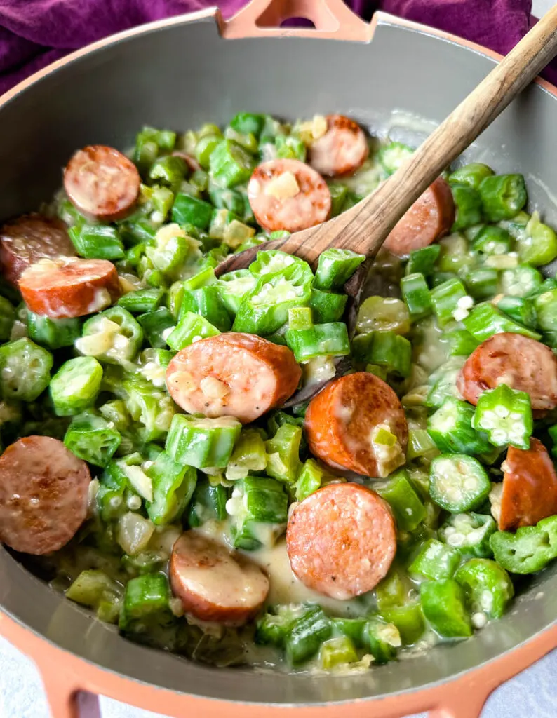 smothered okra with sausage and gravy in a skillet with a wooden spoon