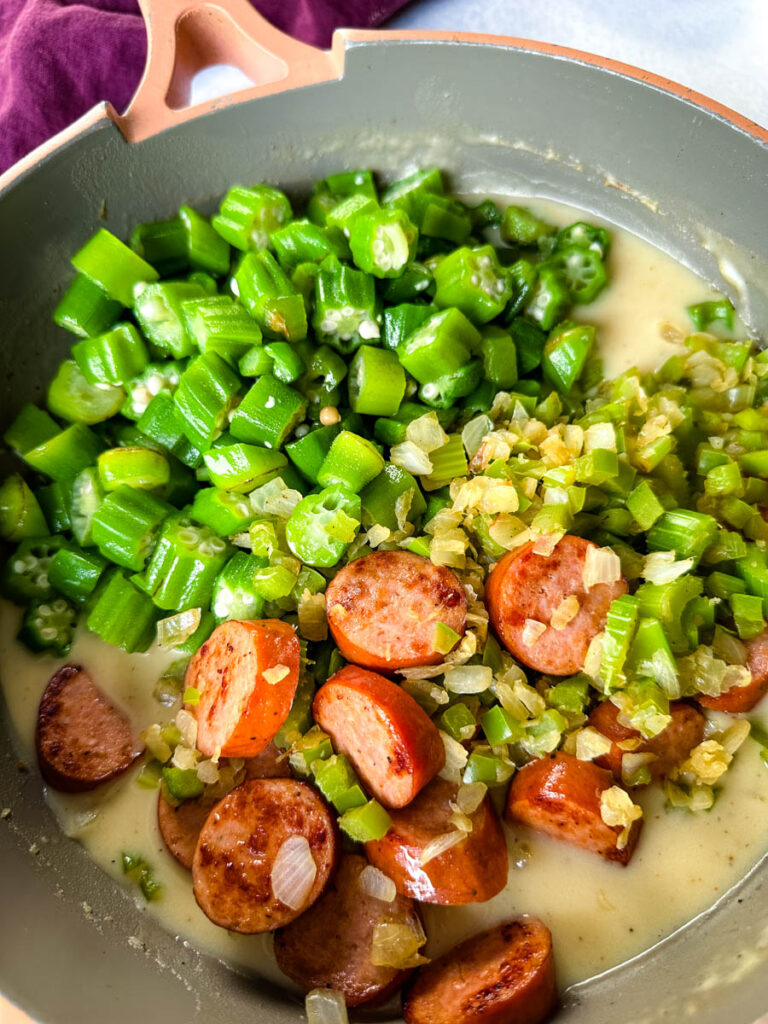 smothered okra with sausage and gravy in a skillet with a wooden spoon