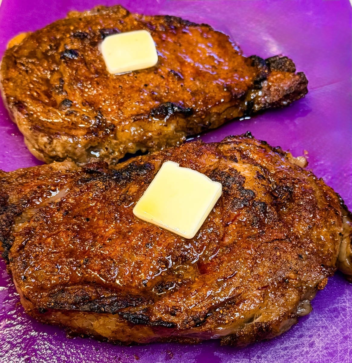 Close-up of two juicy air fryer ribeye steaks finished with butter, showing a caramelized crust and flavorful seasoning.