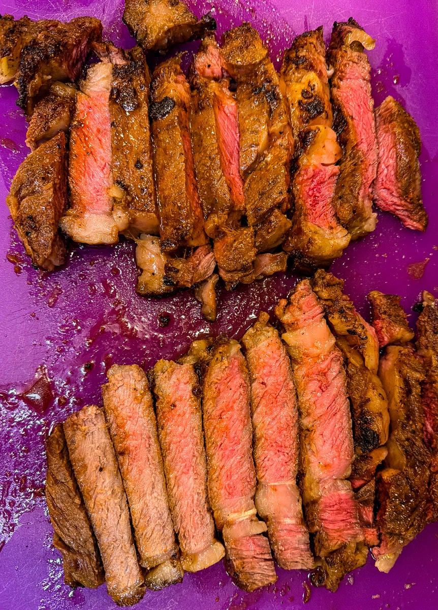 Thick slices of air fryer ribeye steak arranged on a cutting board, showcasing a tender medium-rare interior and golden-brown crust.