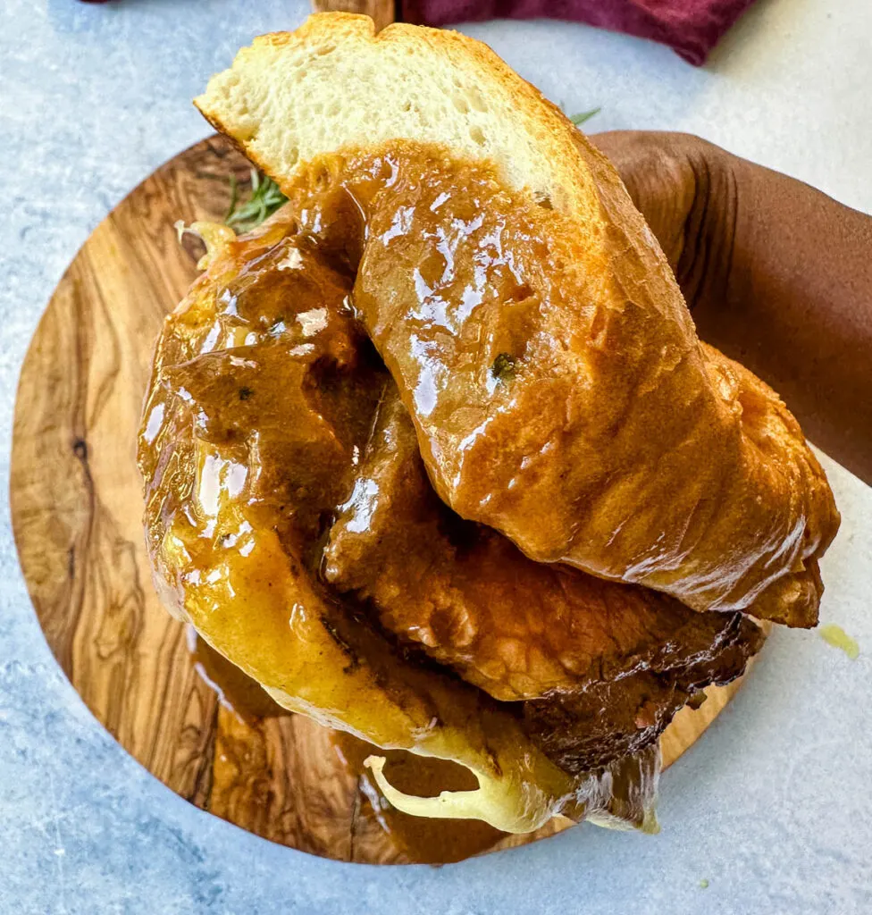 person holding French dip roast beef sandwich dripped in au jus sauce