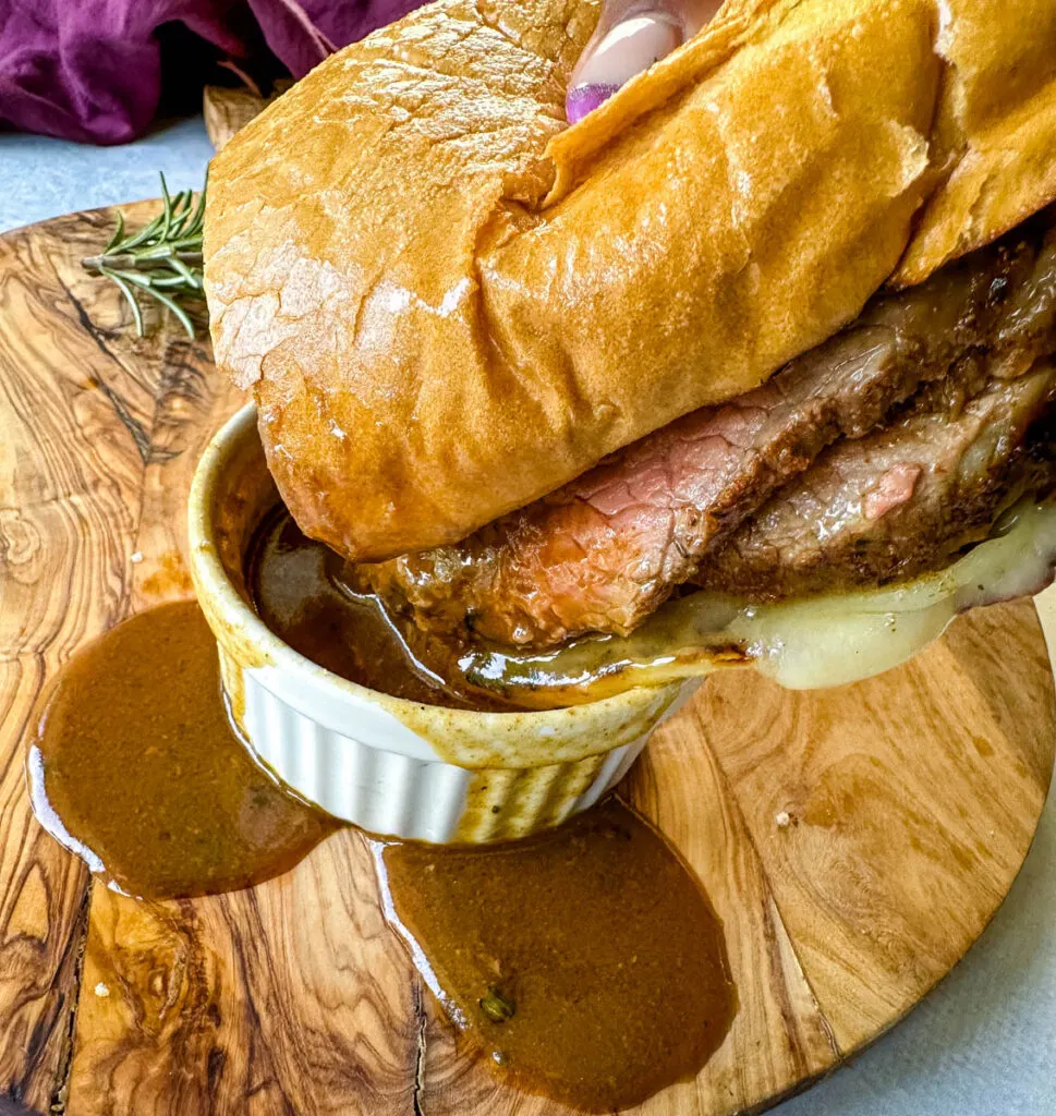 person holding French dip roast beef sandwich dripped in au jus sauce