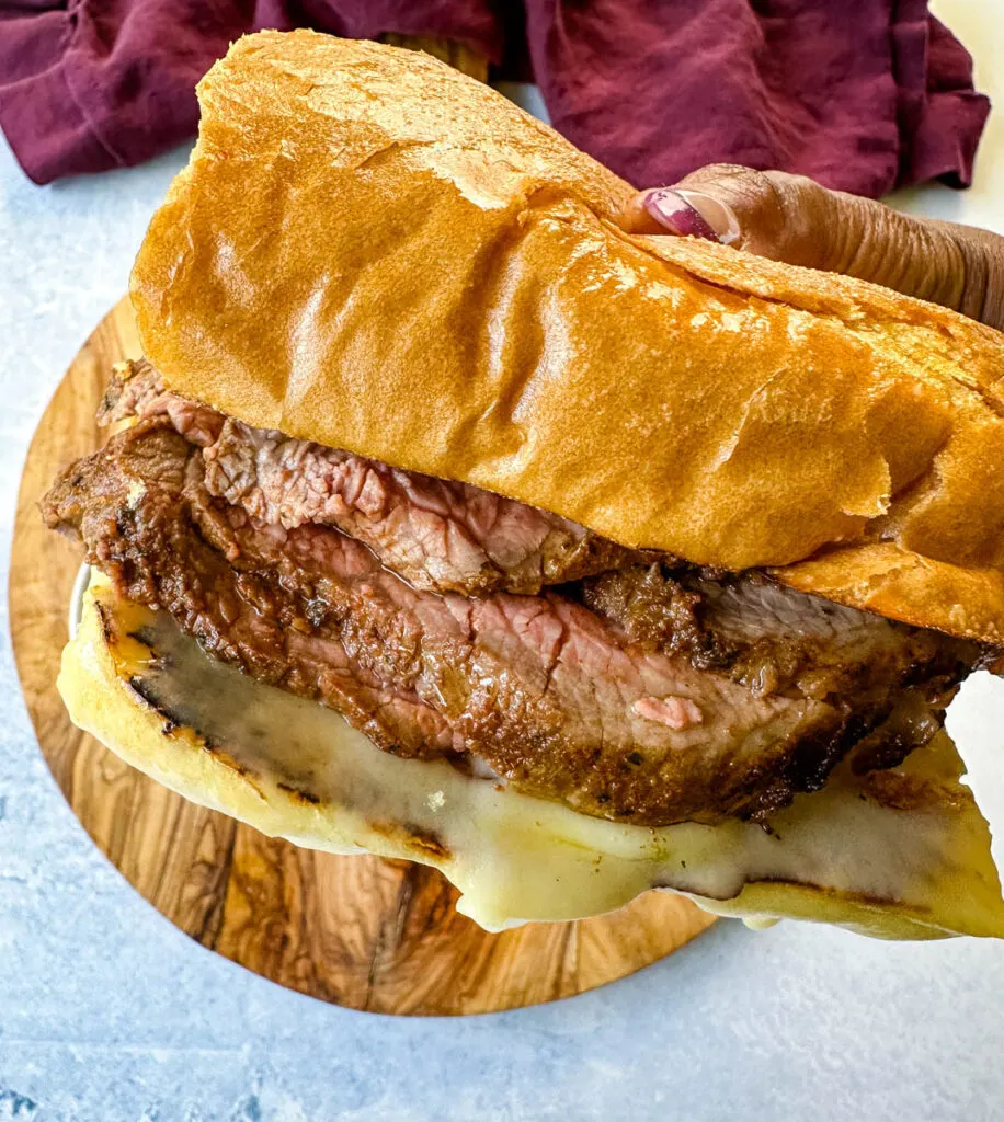 person holding roast beef sandwich with swiss cheese