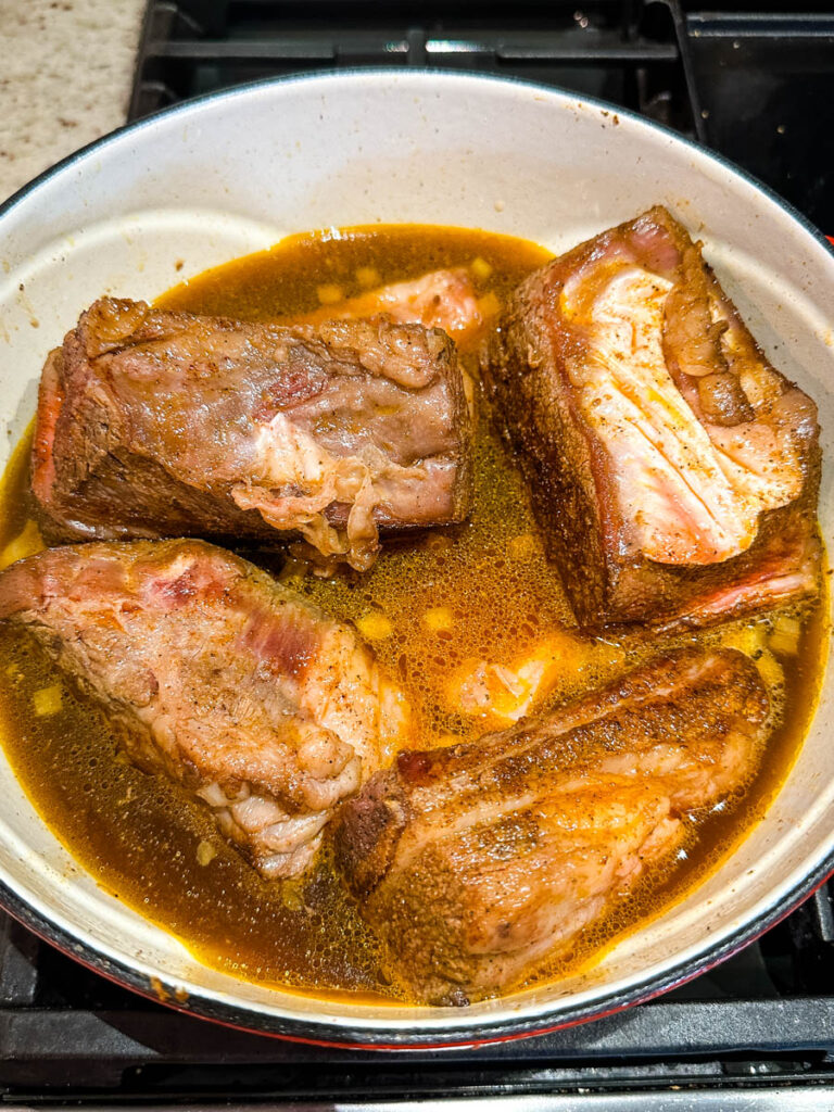 uncooked braised beef short ribs in a Dutch oven with broth