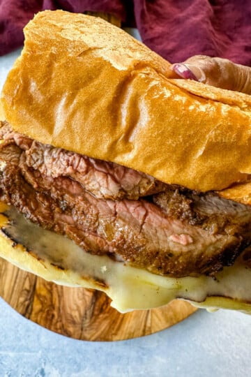 person holding roast beef sandwich with swiss cheese