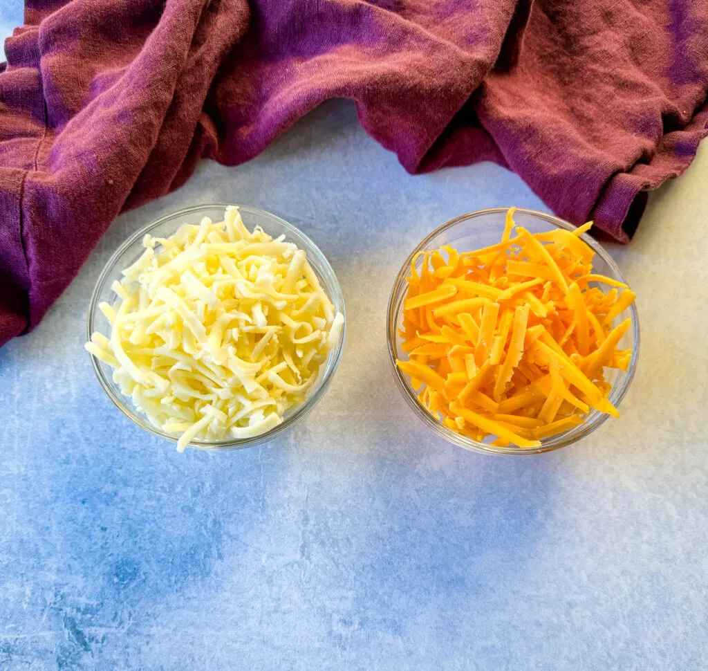 grated mozzarella and grated cheddar cheese in separate glass bowls