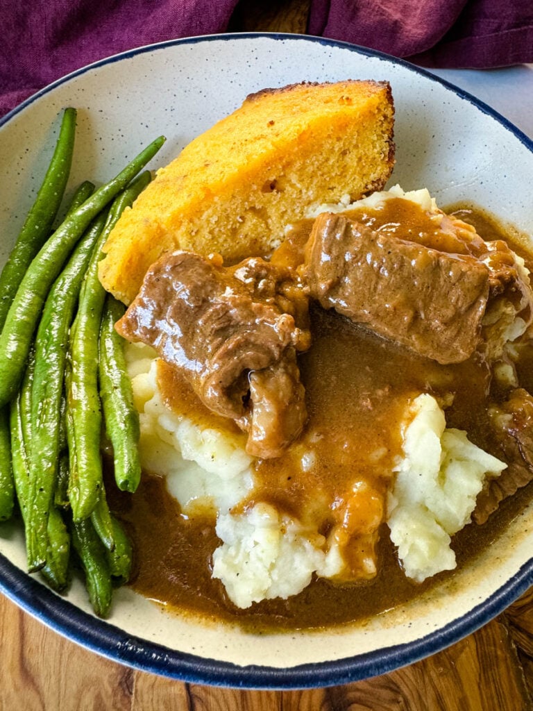 beef tips and gravy with mashed potatoes, green beans and cornbread in a bowl