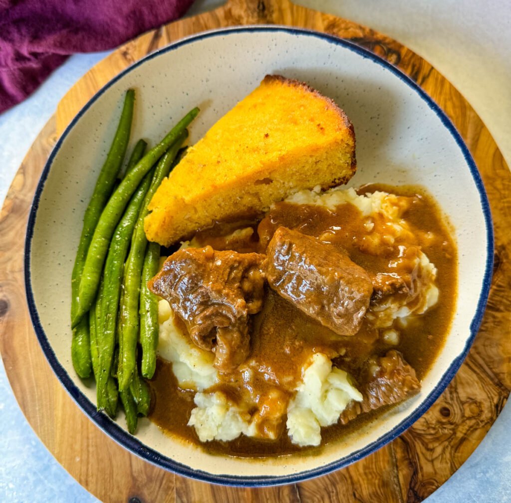 beef tips and gravy with mashed potatoes, green beans and cornbread in a bowl