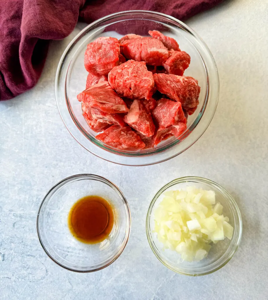 raw beef tips stew meat, diced white onions, and worcestershire sauce in separate glass bowls