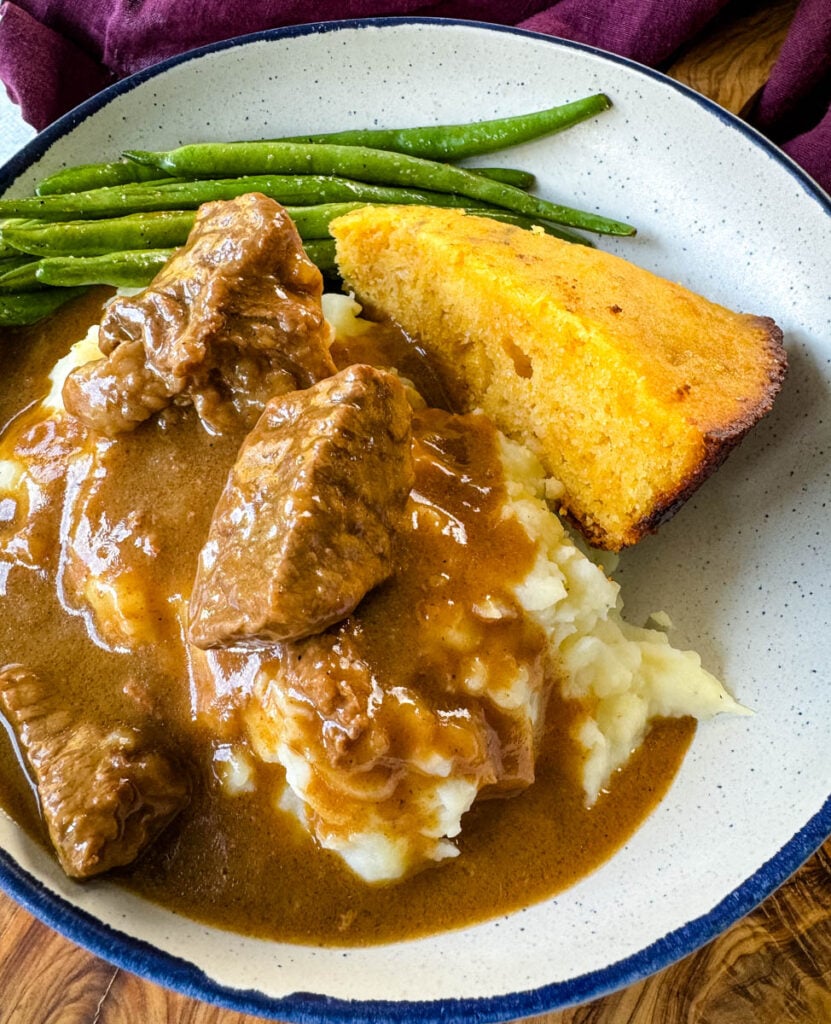 beef tips and gravy with mashed potatoes, green beans and cornbread in a bowl