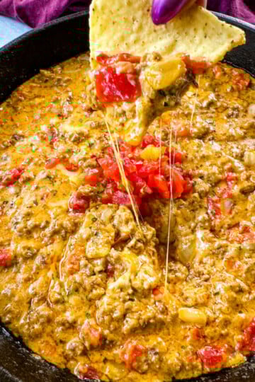 person holding chip with Rotel cheese dip with ground beef in a skillet