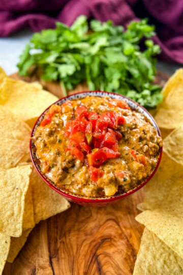 Rotel cheese dip with ground beef in a bowl with a plate of chips and cilantro
