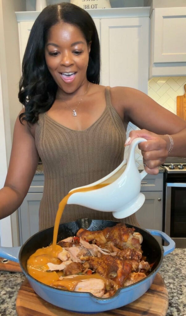 Brandi Crawford pours homemade turkey gravy from a white gravy boat over roasted turkey in a skillet.
