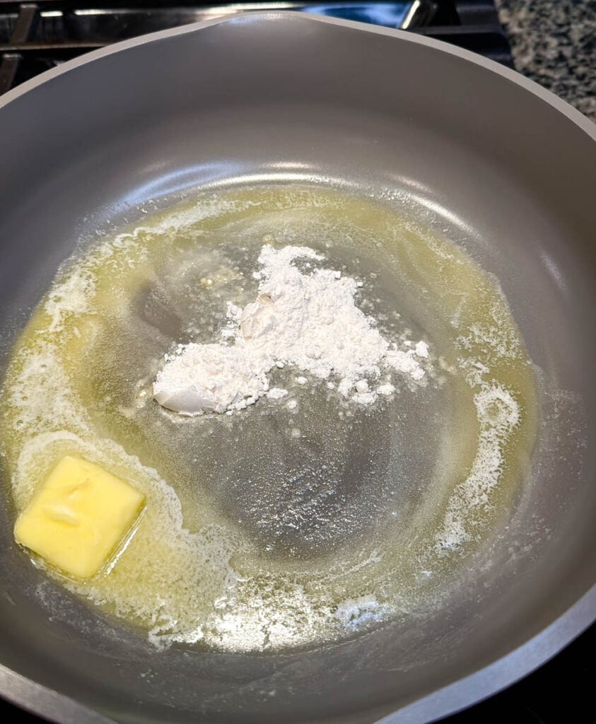 Flour is added to melted butter in a skillet to make a roux for turkey gravy from drippings.