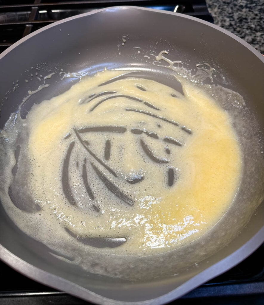 Flour and butter cook together in a skillet to form a roux for homemade turkey gravy.