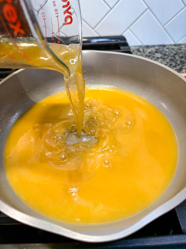 Turkey drippings are poured from a glass measuring cup into a skillet to begin making homemade turkey gravy.
