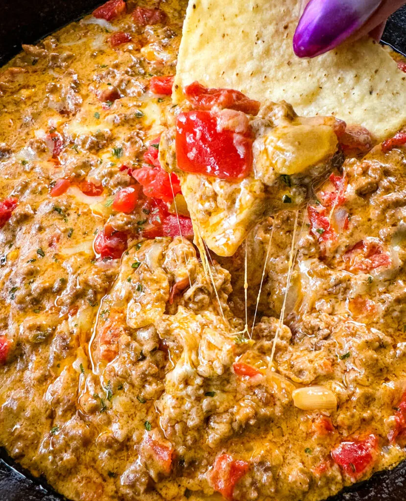 person holding chip with Rotel cheese dip with ground beef in a skillet