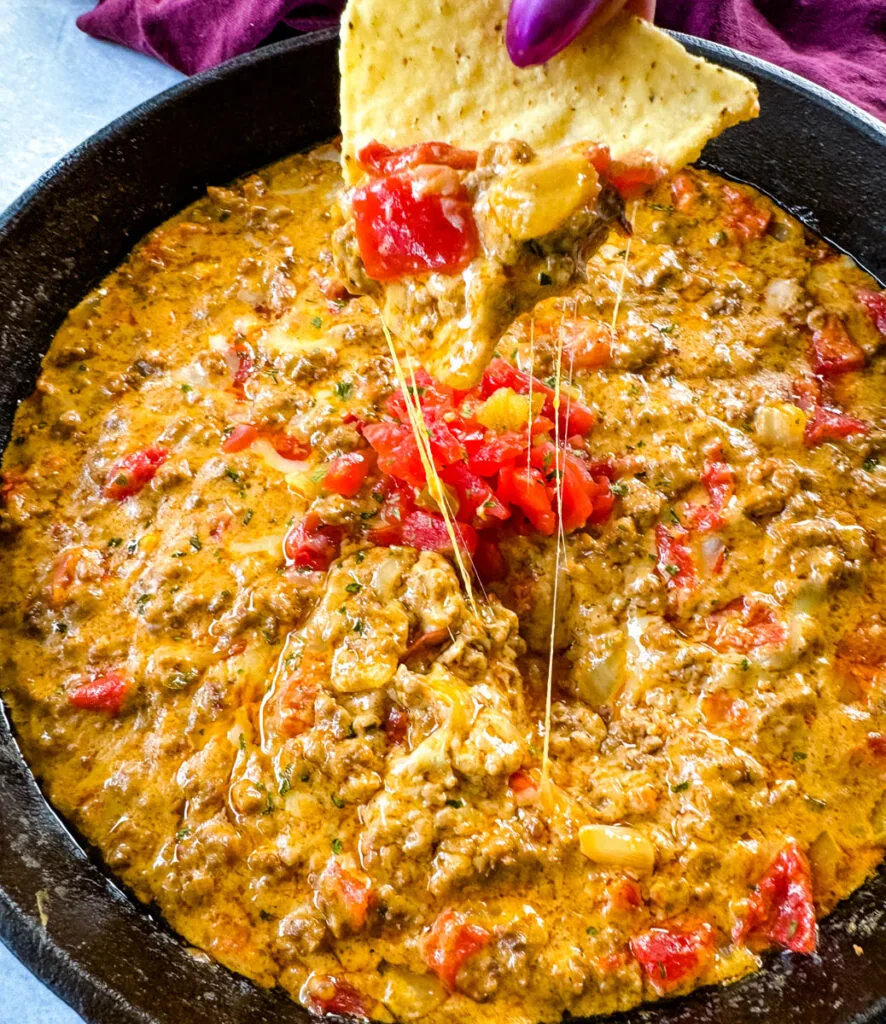 person holding chip with Rotel cheese dip with ground beef in a skillet
