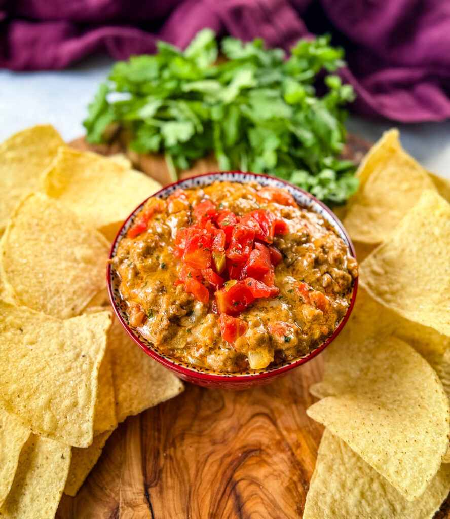 Rotel cheese dip with ground beef in a bowl with a plate of chips and cilantro