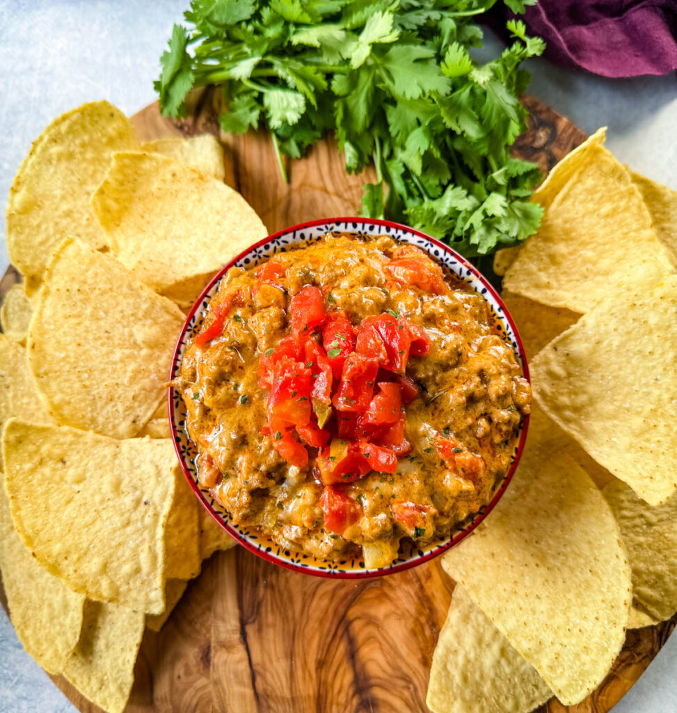 Rotel cheese dip with ground beef in a bowl with a plate of chips and cilantro