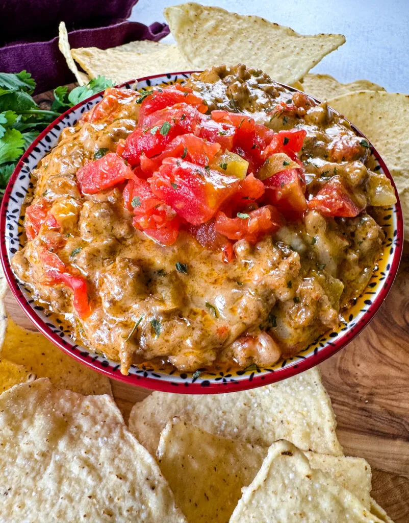 Rotel cheese dip with ground beef in a bowl with a plate of chips and cilantro