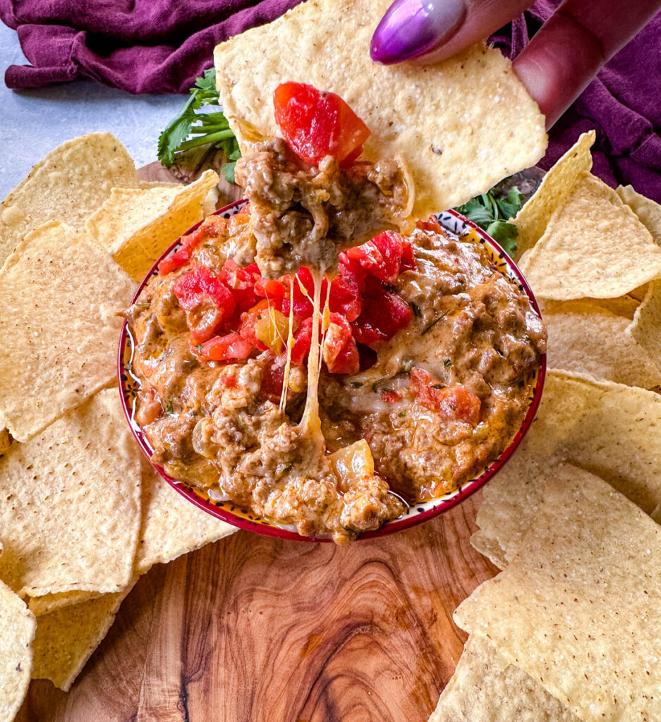 Rotel cheese dip with ground beef in a bowl with a plate of chips and cilantro