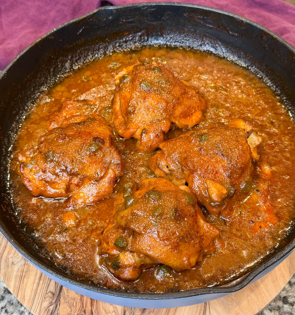 Four smothered chicken thighs simmering in a cast iron skillet filled with thick Southern-style brown gravy.