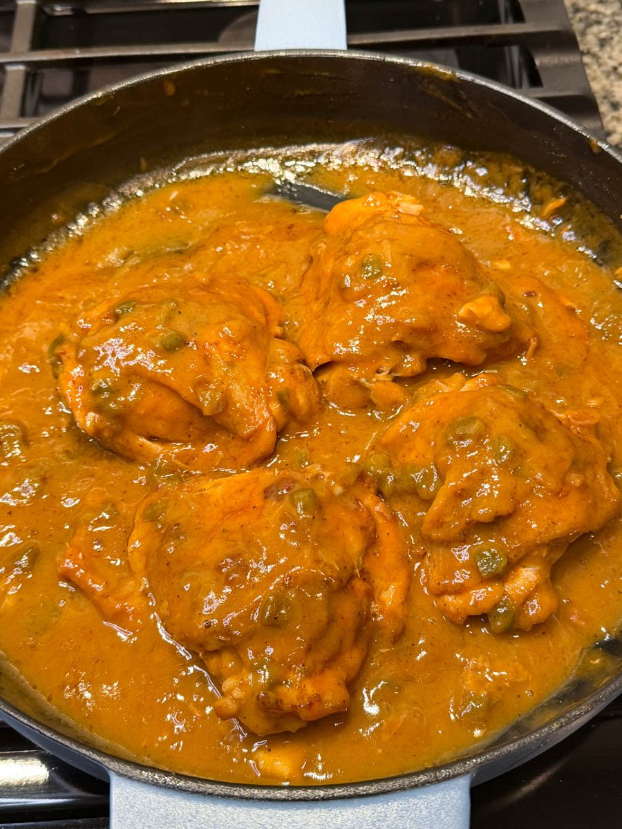 Chicken thighs simmering in a thick brown smothered chicken gravy inside a skillet on the stovetop.