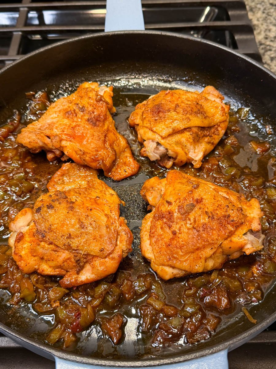 Seasoned chicken thighs browned in a skillet with sautéed onions and green bell peppers to build the base for smothered chicken.
