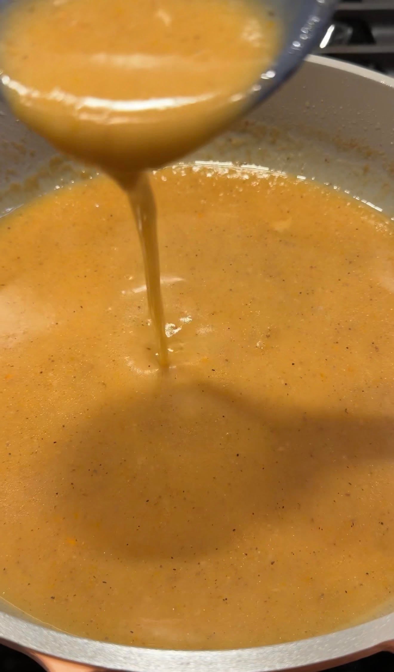 Smooth homemade turkey gravy made from drippings pours from a ladle back into the pan, showing its rich, silky consistency.