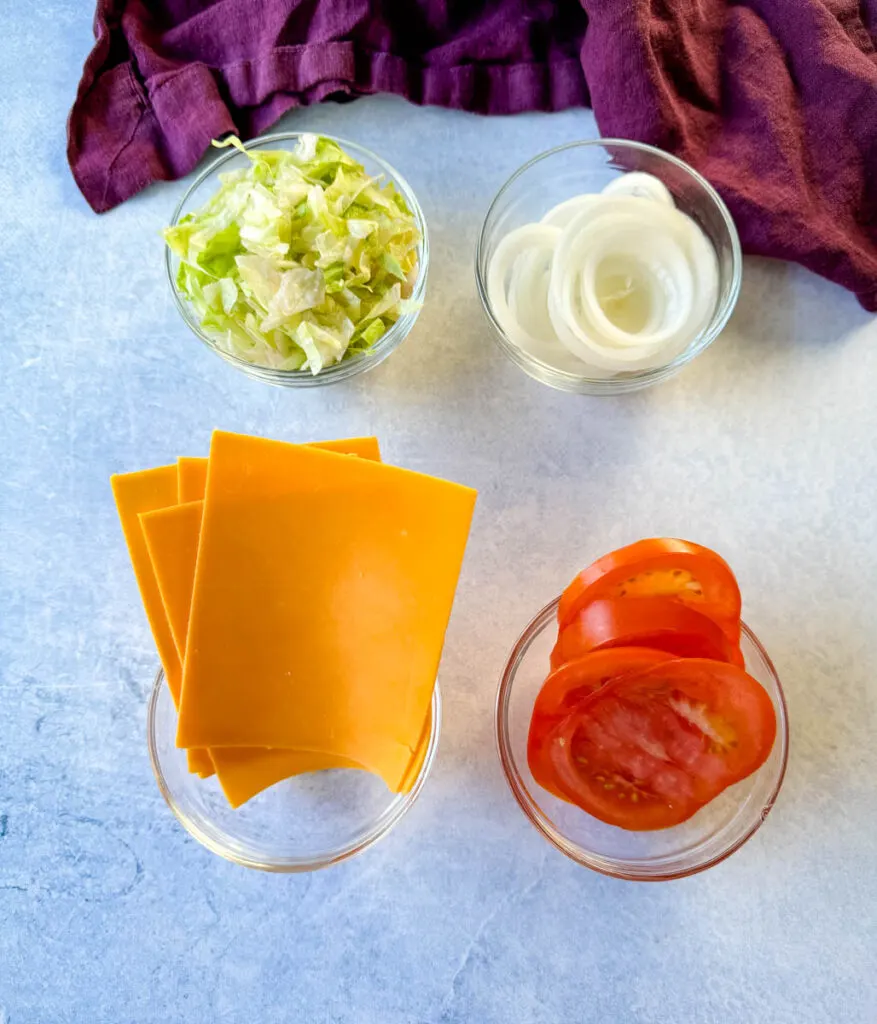 shredded lettuce, sliced onions, sliced cheese, and sliced tomatoes in separate glass bowls