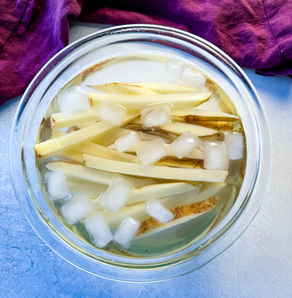 sliced potatoes with water and ice in a glass bowl