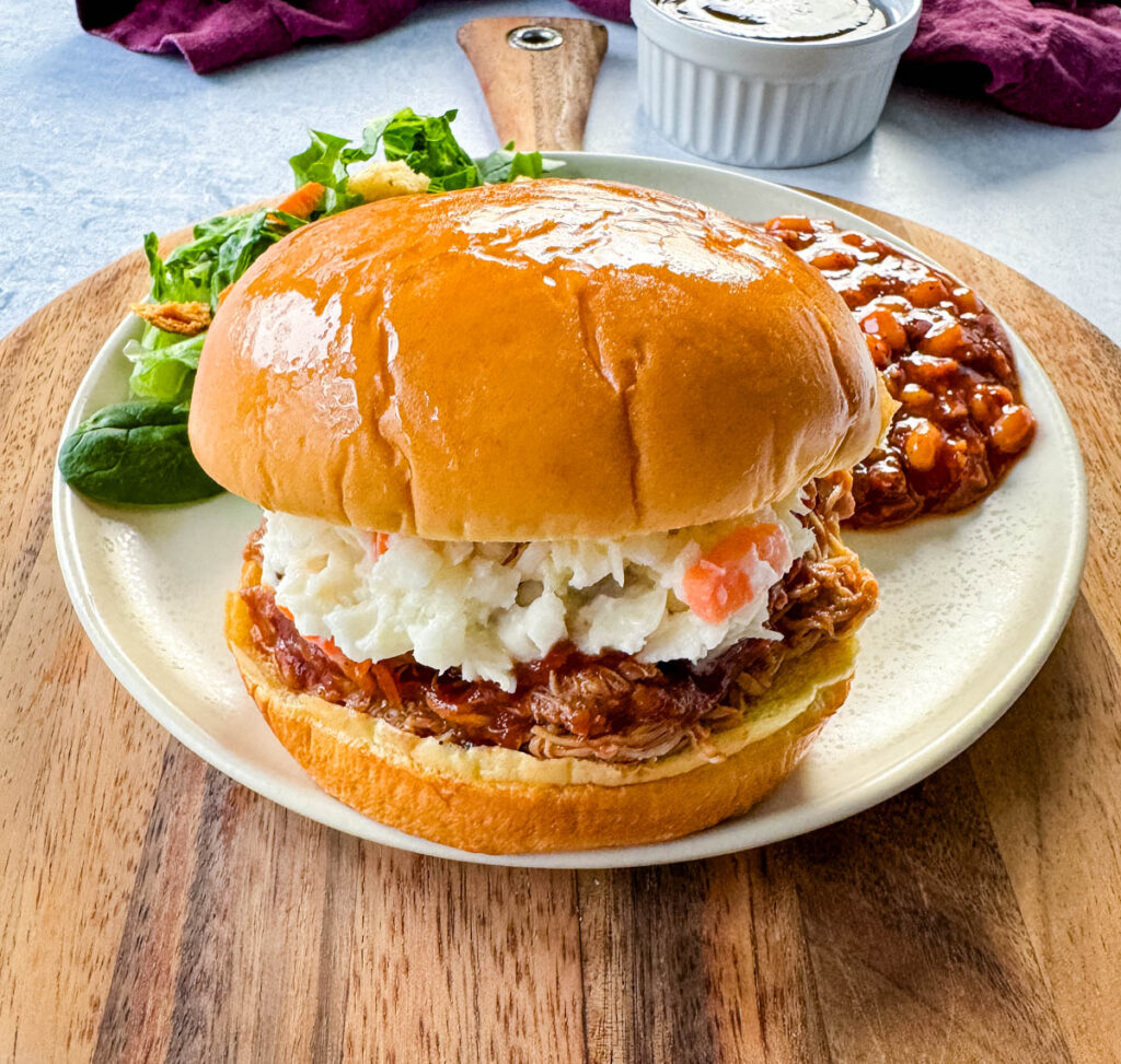 slow cooker Crockpot pulled chicken sandwich with BBQ sauce and coleslaw on a plate with baked beans