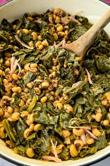 collard greens and black eyed peas with smoked turkey in a red Dutch oven with a wooden spoon