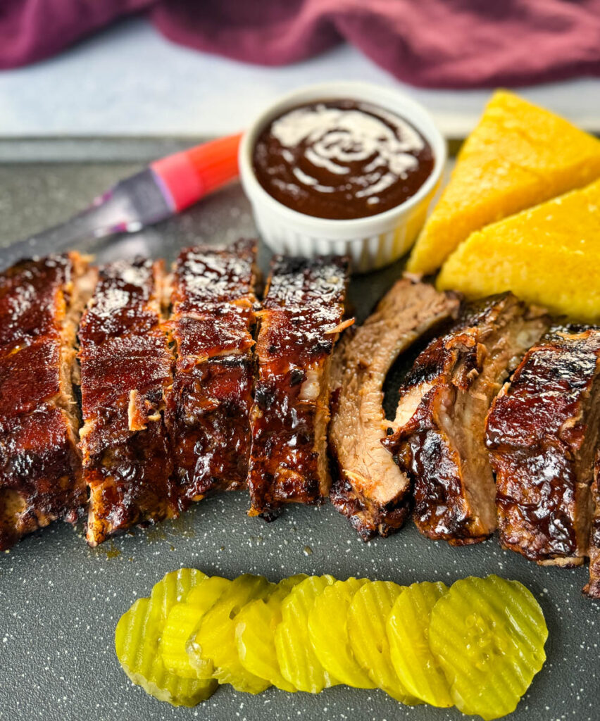 cooked ribs with BBQ sauce on a plate with cornbread and pickles